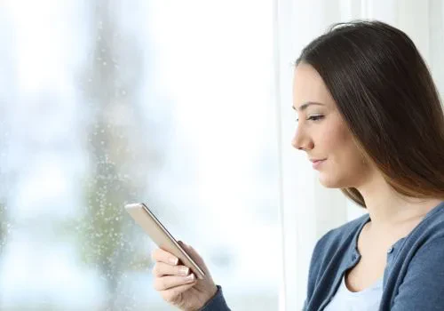 A woman playing a game on her cellphone while it’s raining on her window