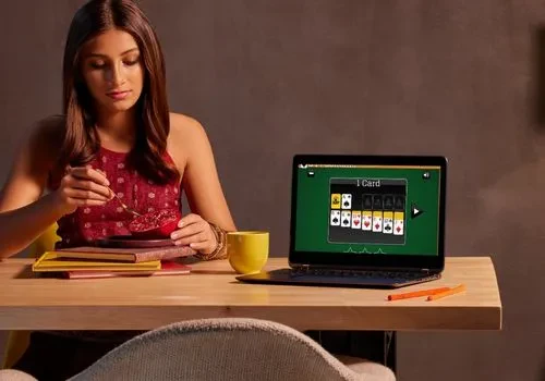 A solo woman eating a snack while an open game of solitaire from 247 Solitaire can be seen on her laptop