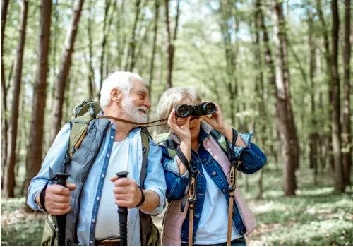An elderly couple bird watching as a hobby with full gear and binoculars